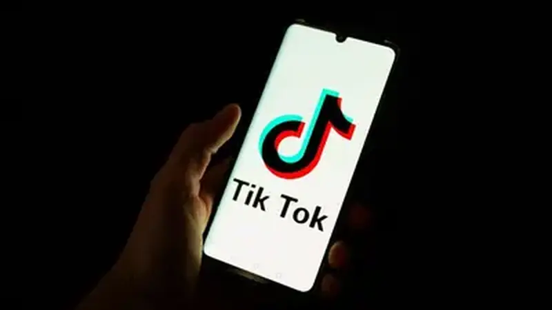 Hand holding a smartphone showing the TikTok logo in the dark